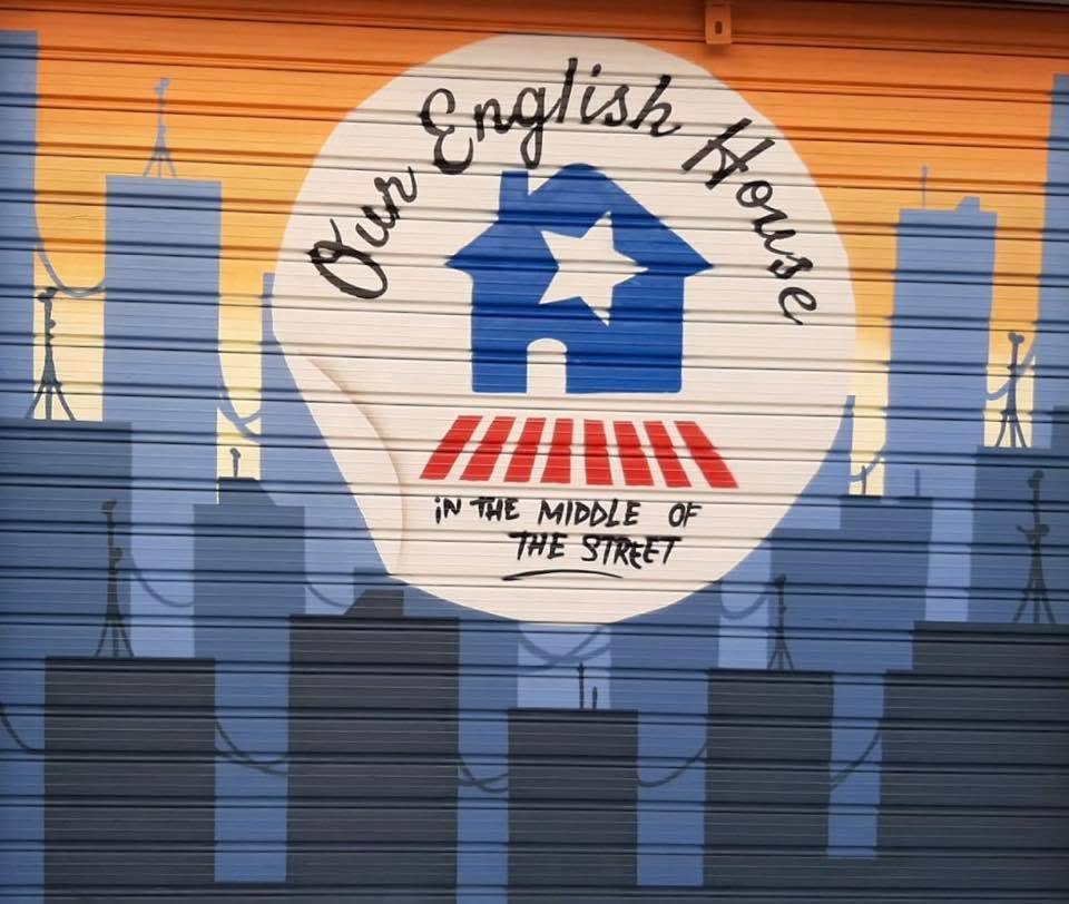 Persiana de la academia con el logo de Our English House pintado sobre una ciudad al atardecer